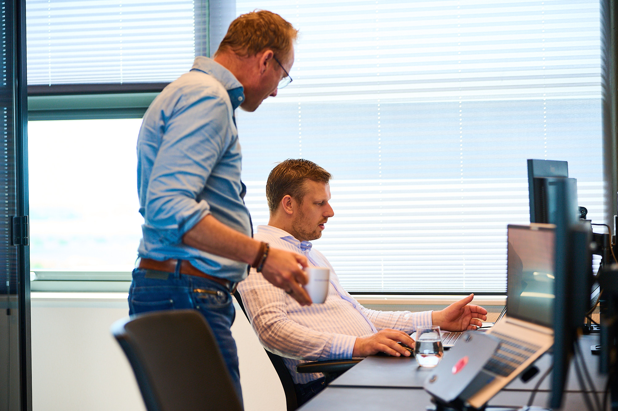 Collega's Michel en Giovanni met elkaar in gesprek achter Giovanni zijn laptop
